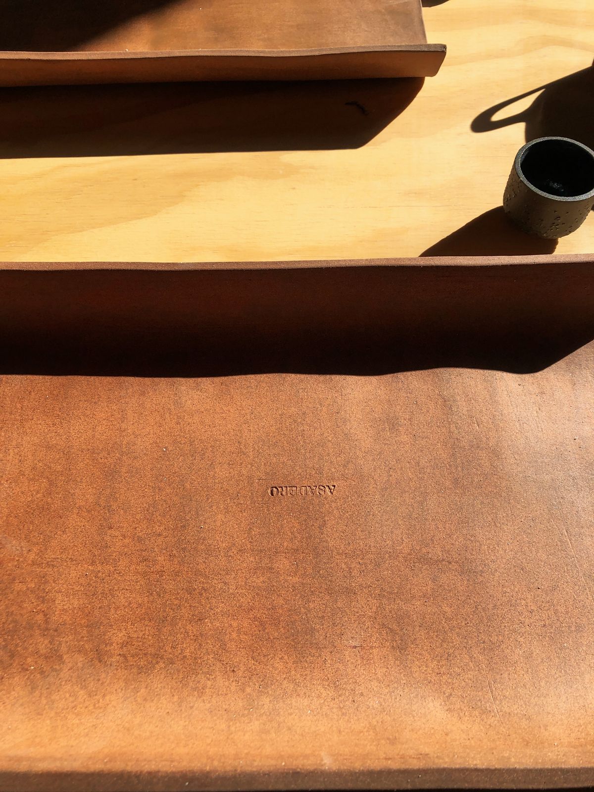 Leather placemat embossed with the Asadero logo on a wooden table