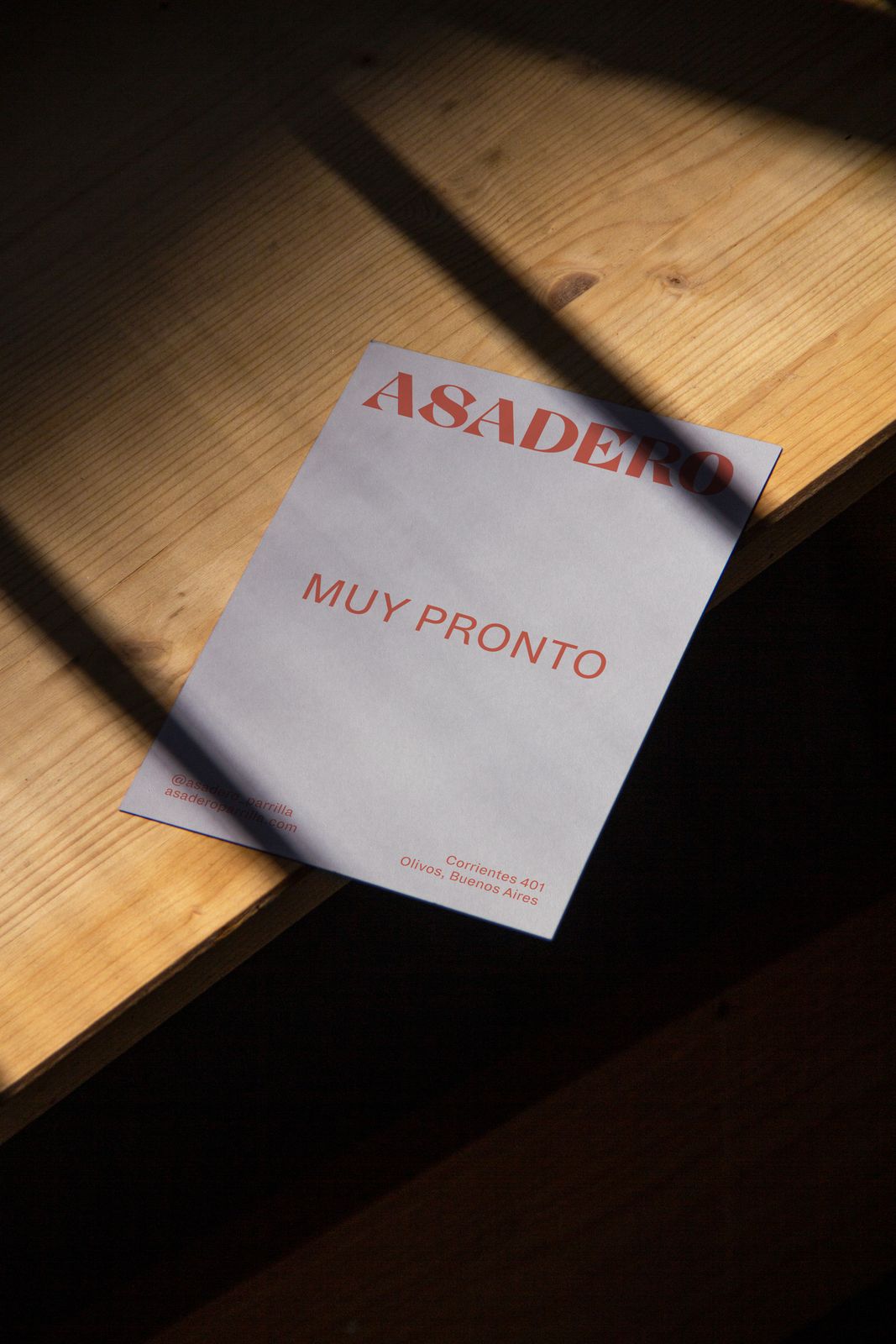 Asadero Muy Pronto opening flyer on a wooden bench in sunlight