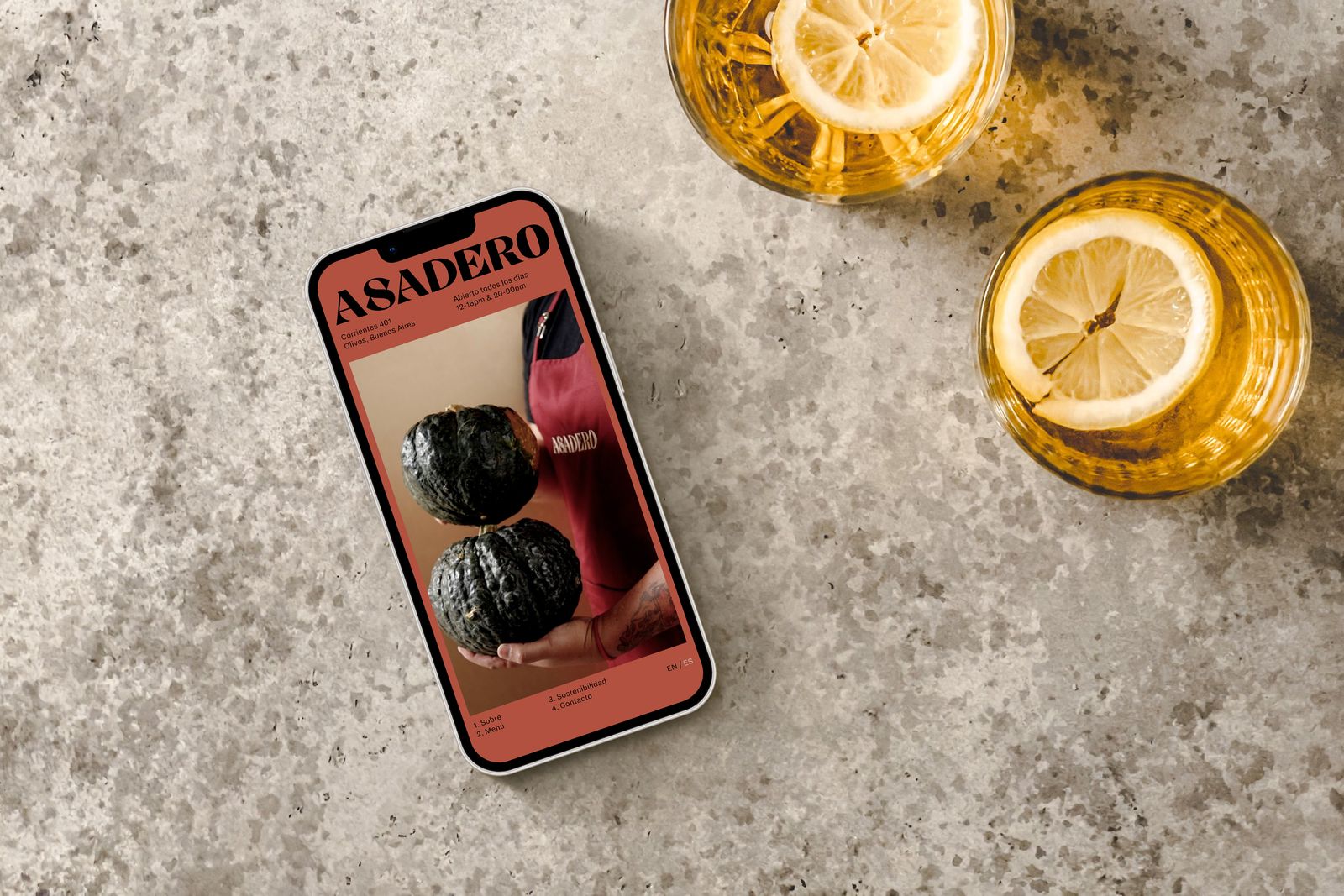 Asadero website on a phone lying on a stone table next to two drinks with lemon