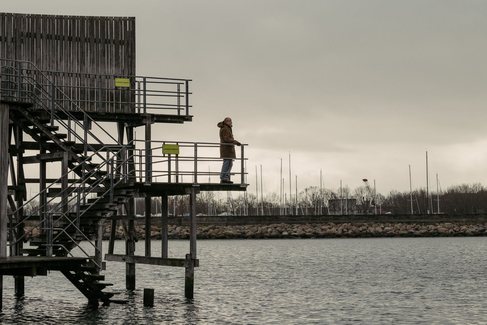 Figure on a wooden platform above the grey Copenhagen waterfront