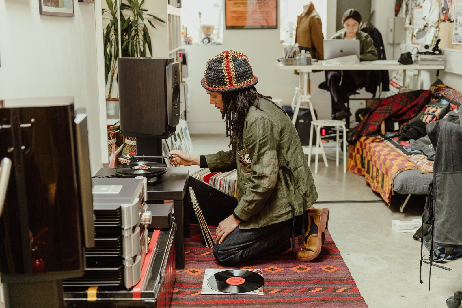 Designer kneeling by a record player and speakers on a patterned rug
