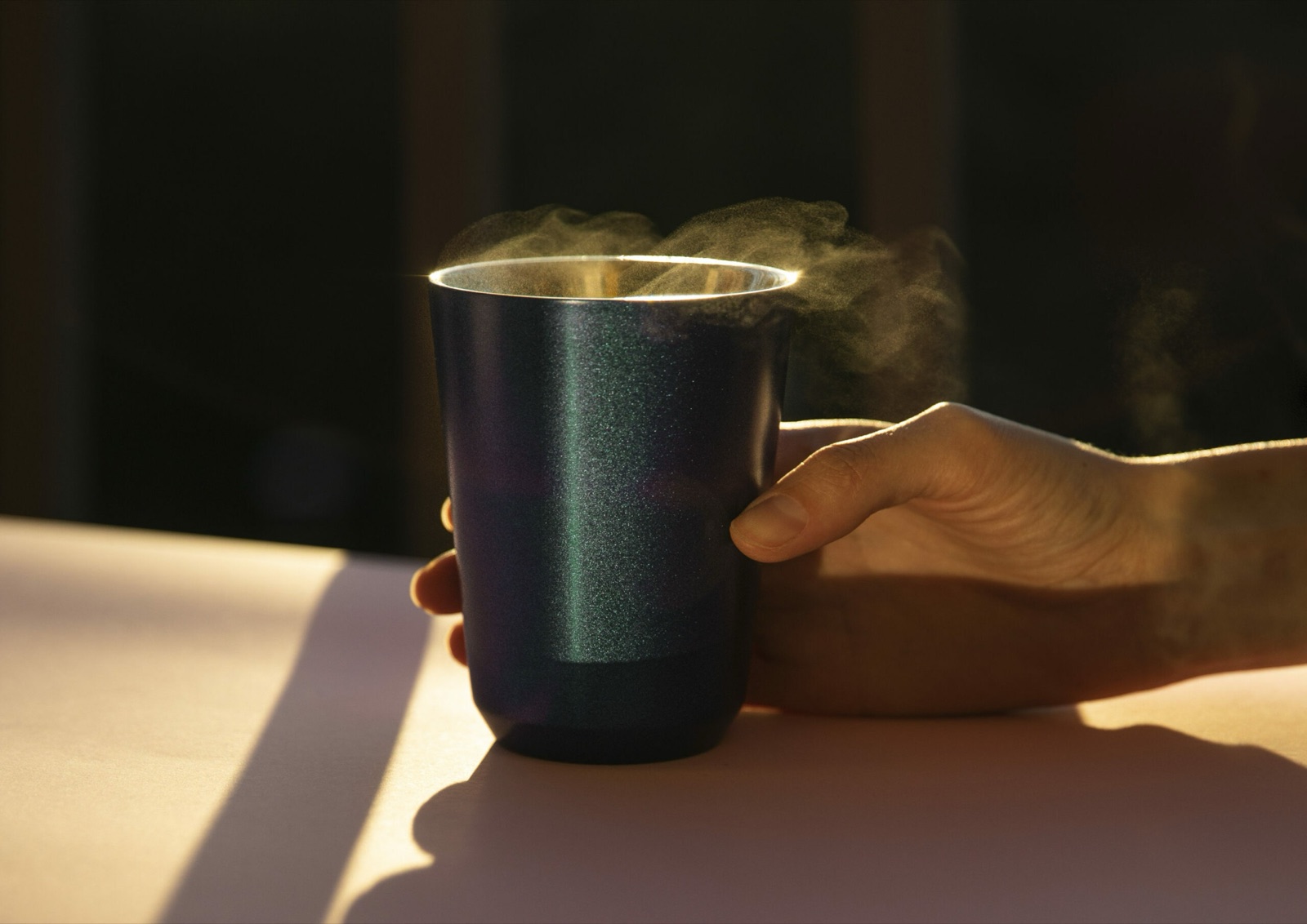 Hand resting on a dark Meama coffee cup in warm evening sunlight
