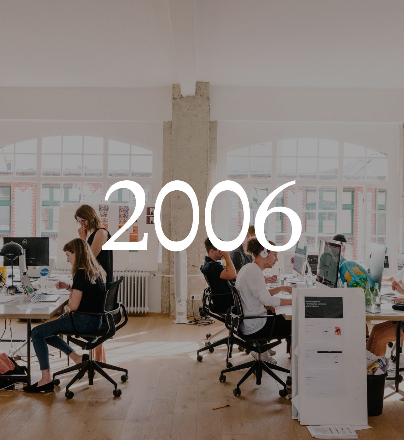 The NoMoreSleep studio in Berlin with people working at desks under arched windows, with the year 2006 set over the image