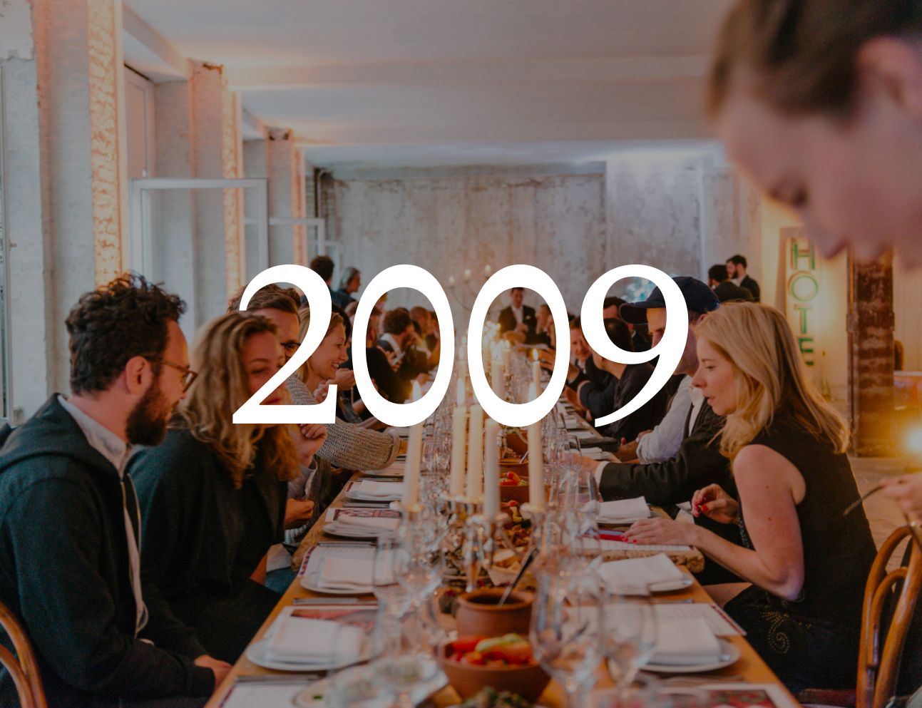 Long candlelit dinner table with guests, with the year 2009 set over the image