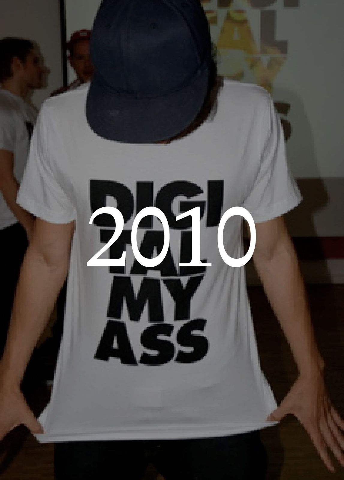 Person in a cap holding out a white T-shirt with a large black slogan, with the year 2010 set over the image