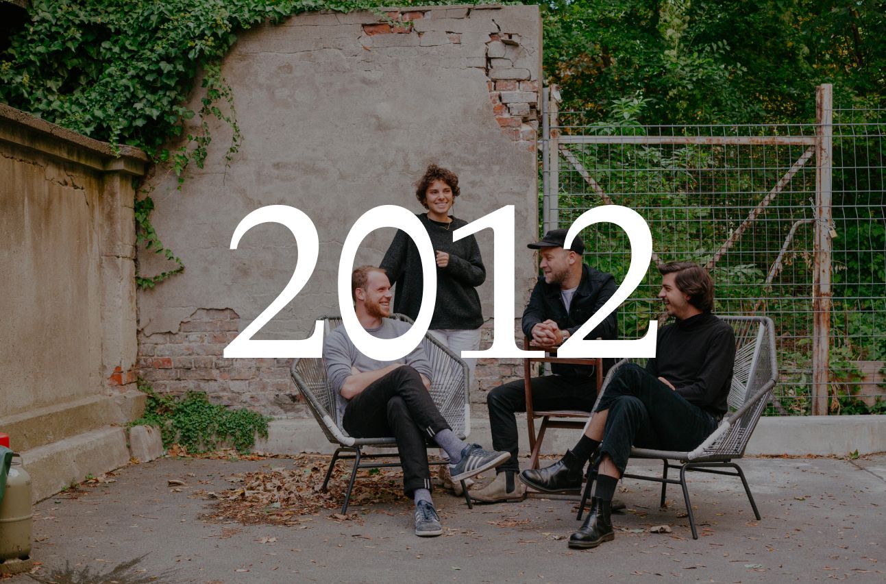 Four people talking on chairs in a Berlin courtyard, with the year 2012 set over the image