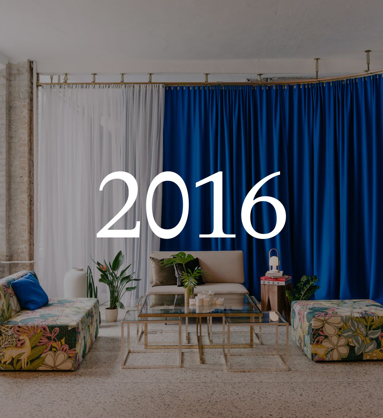 Lounge with white and blue curtains, floral sofas and a glass table, with the year 2016 set over the image