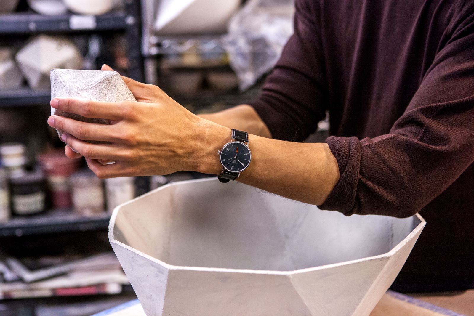 Hands holding a faceted white ceramic bowl, NOMOS watch on the wrist