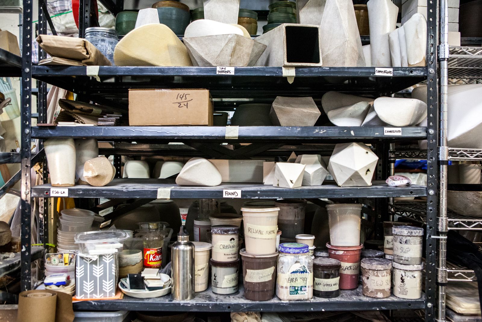 Metal shelves stacked with ceramic moulds and glaze tubs in a New York studio