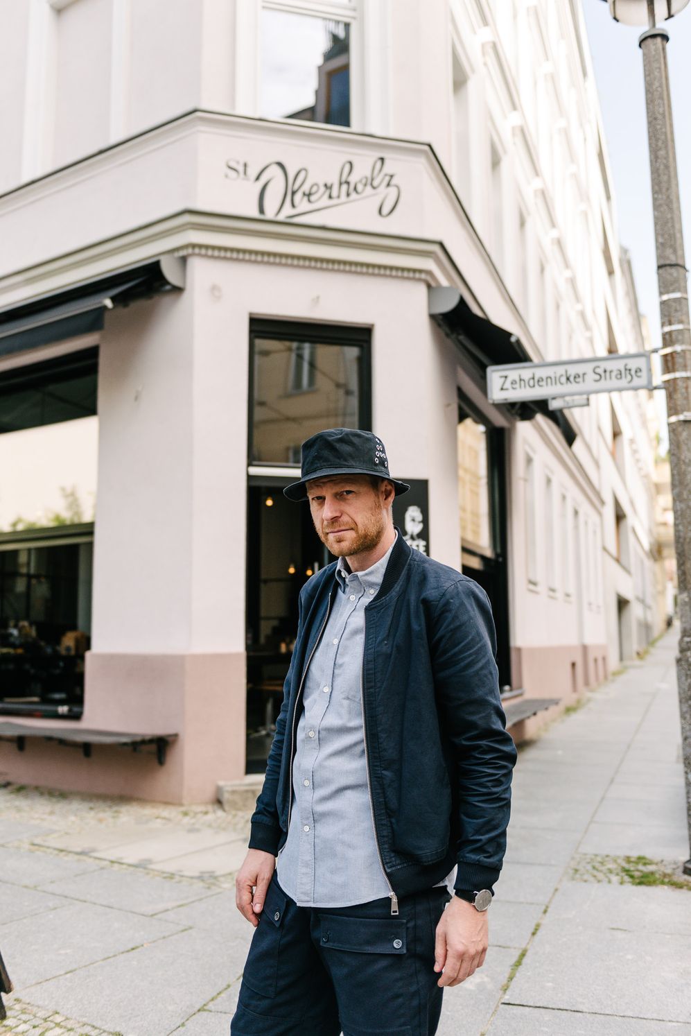 Entrepreneur in a hat standing at the street corner outside his cafe in Berlin-Mitte