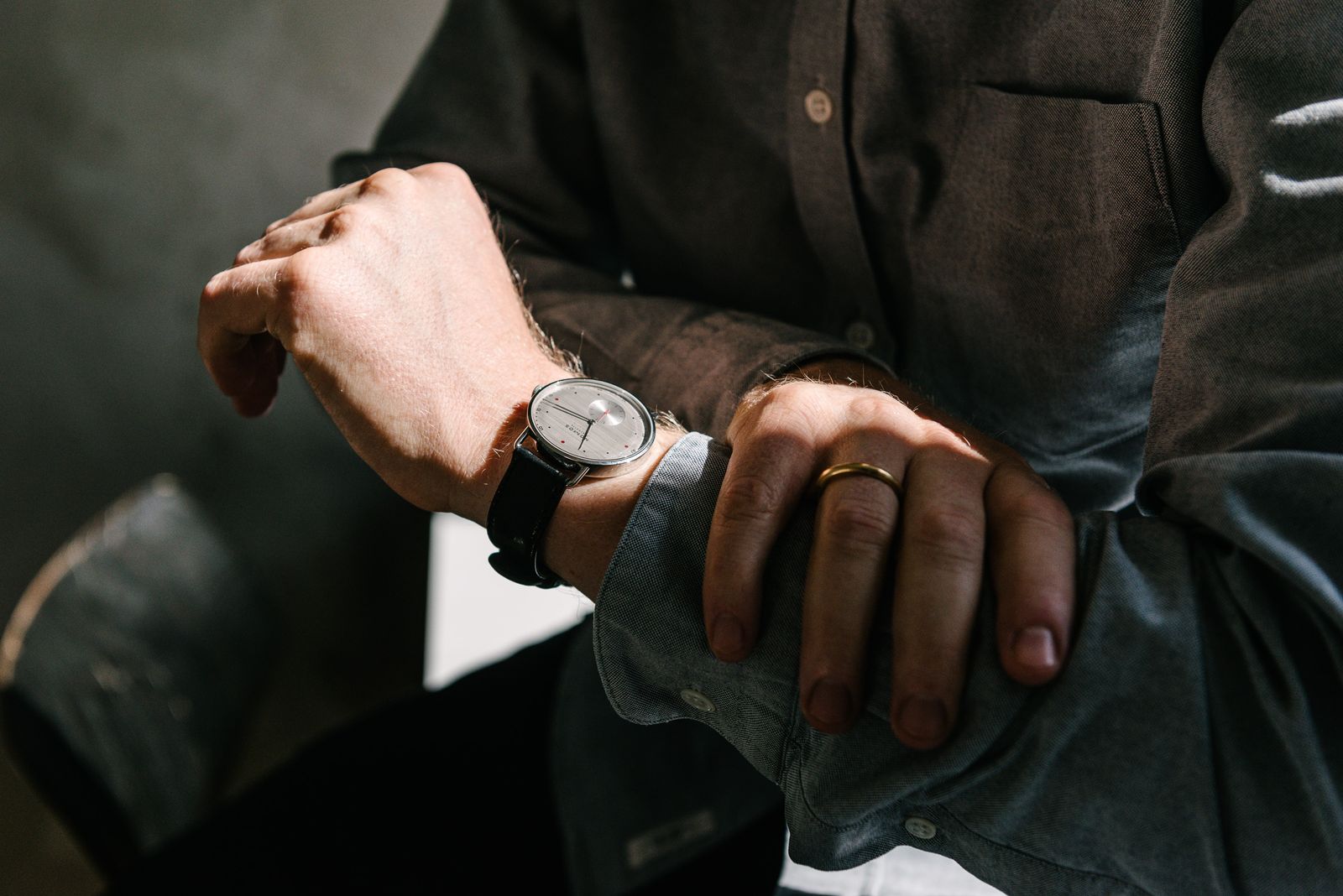 Close-up of a NOMOS watch on a wrist against a dark jacket