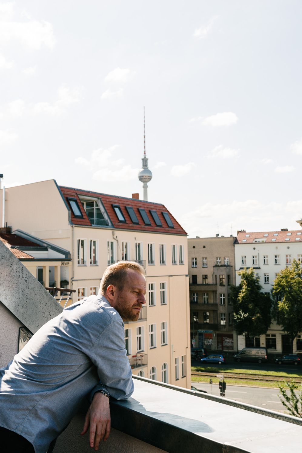 Entrepreneur leaning out of a window with the Berlin TV tower behind rooftops