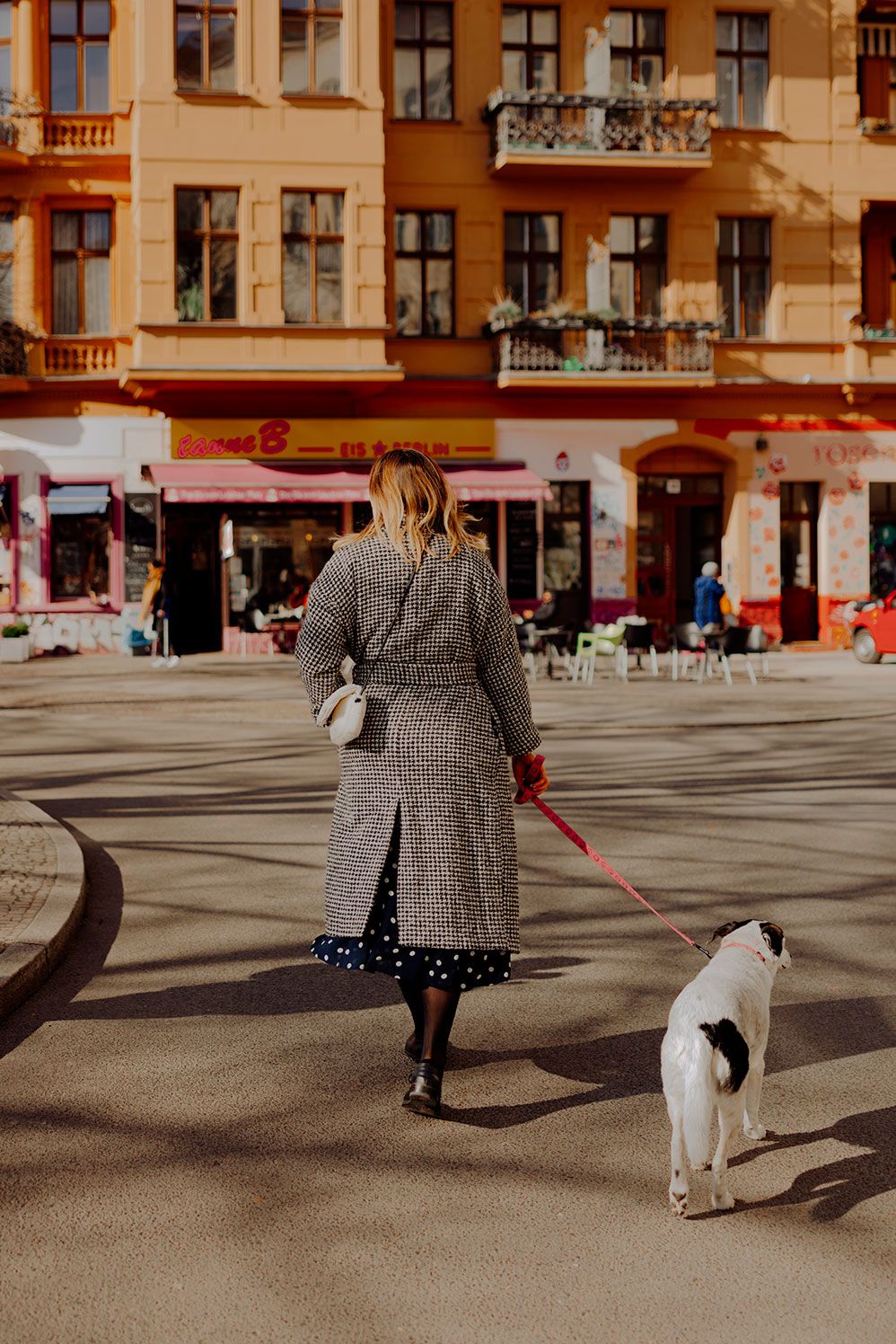 Mary Scherpe walking her dog across a sunny Berlin square