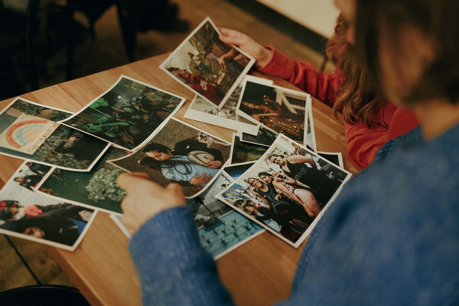 Hands sorting photo prints spread across a wooden table