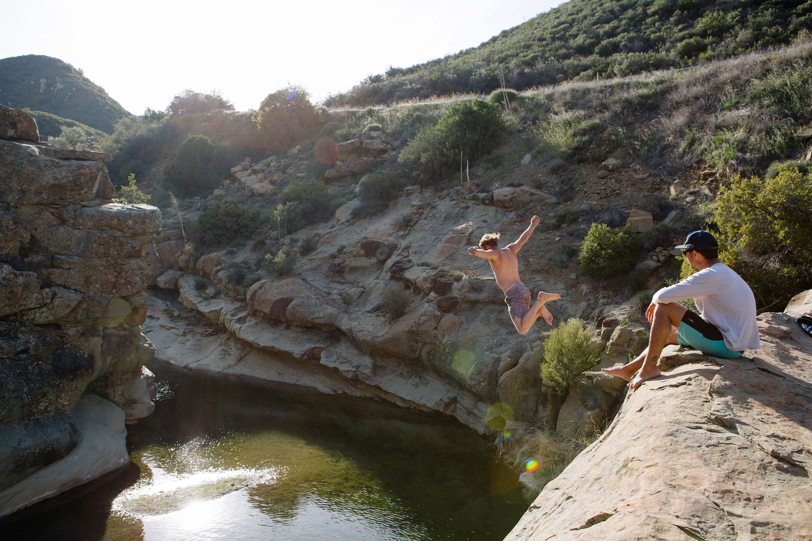 Swimmer jumping from a rock ledge into a mountain swimming hole near Ojai