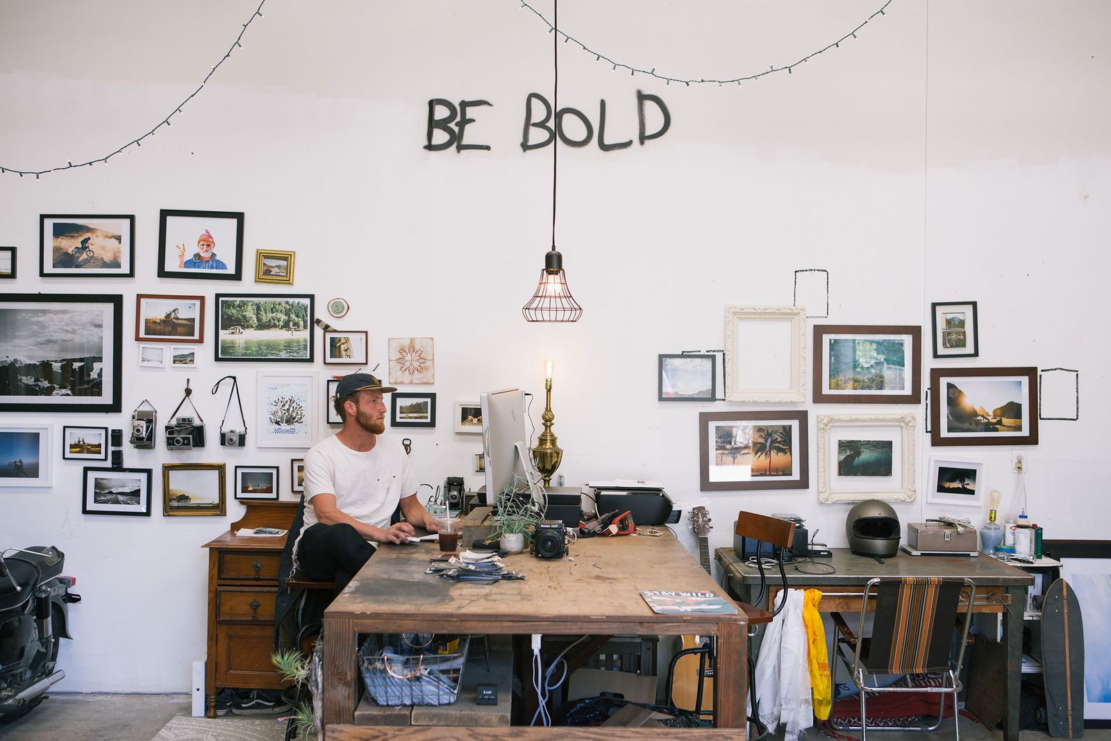 Photographer at his desk in a white warehouse studio hung with framed prints