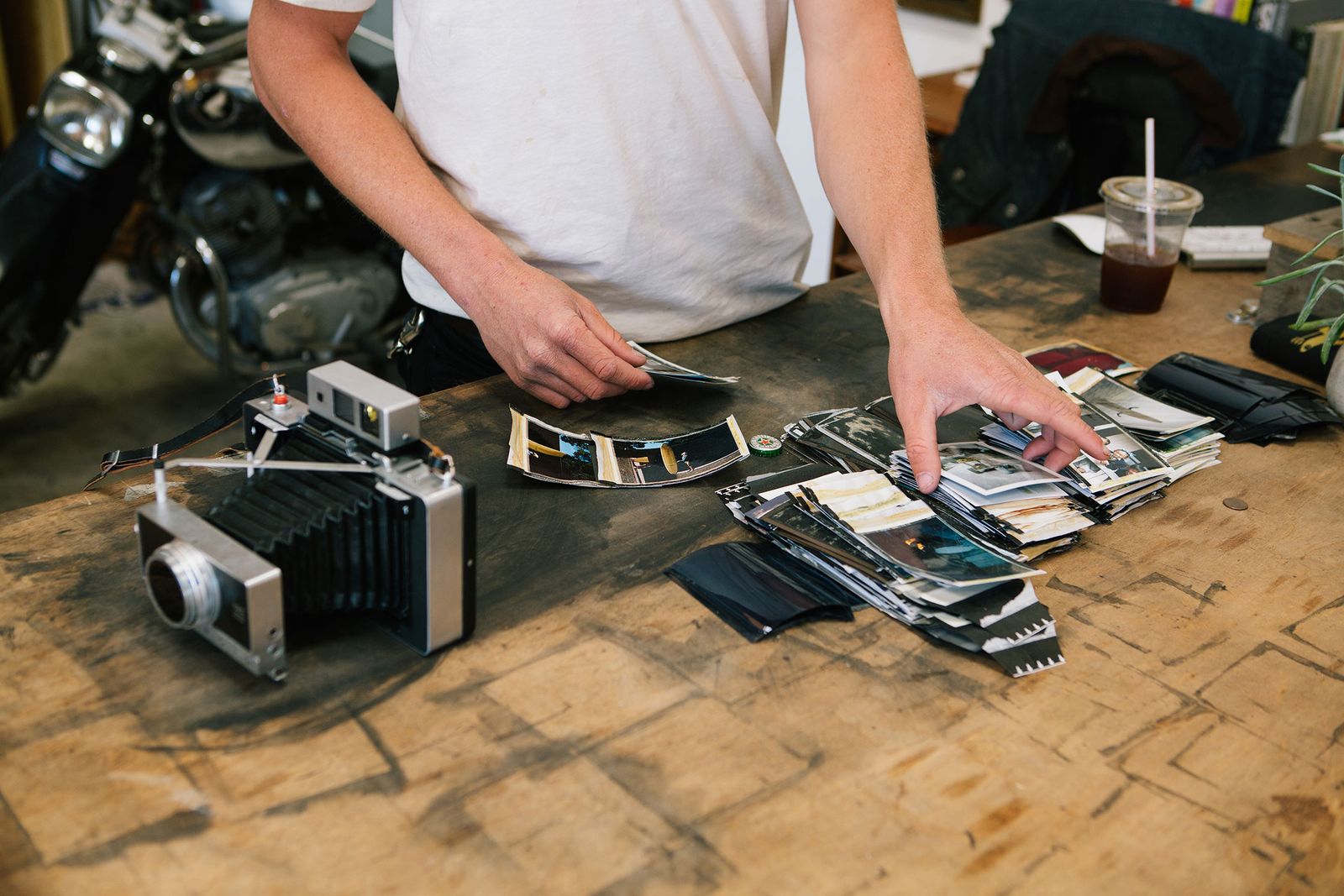 Hands sorting Polaroid prints next to a large-format camera on a wooden table