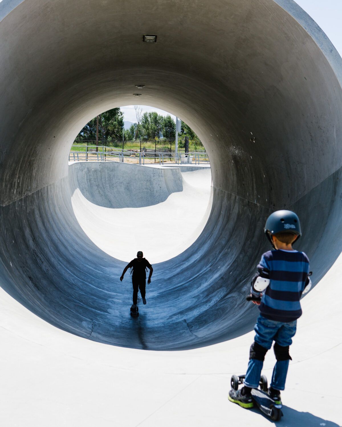 Father and son skating through a concrete full pipe at a San Jose skate park