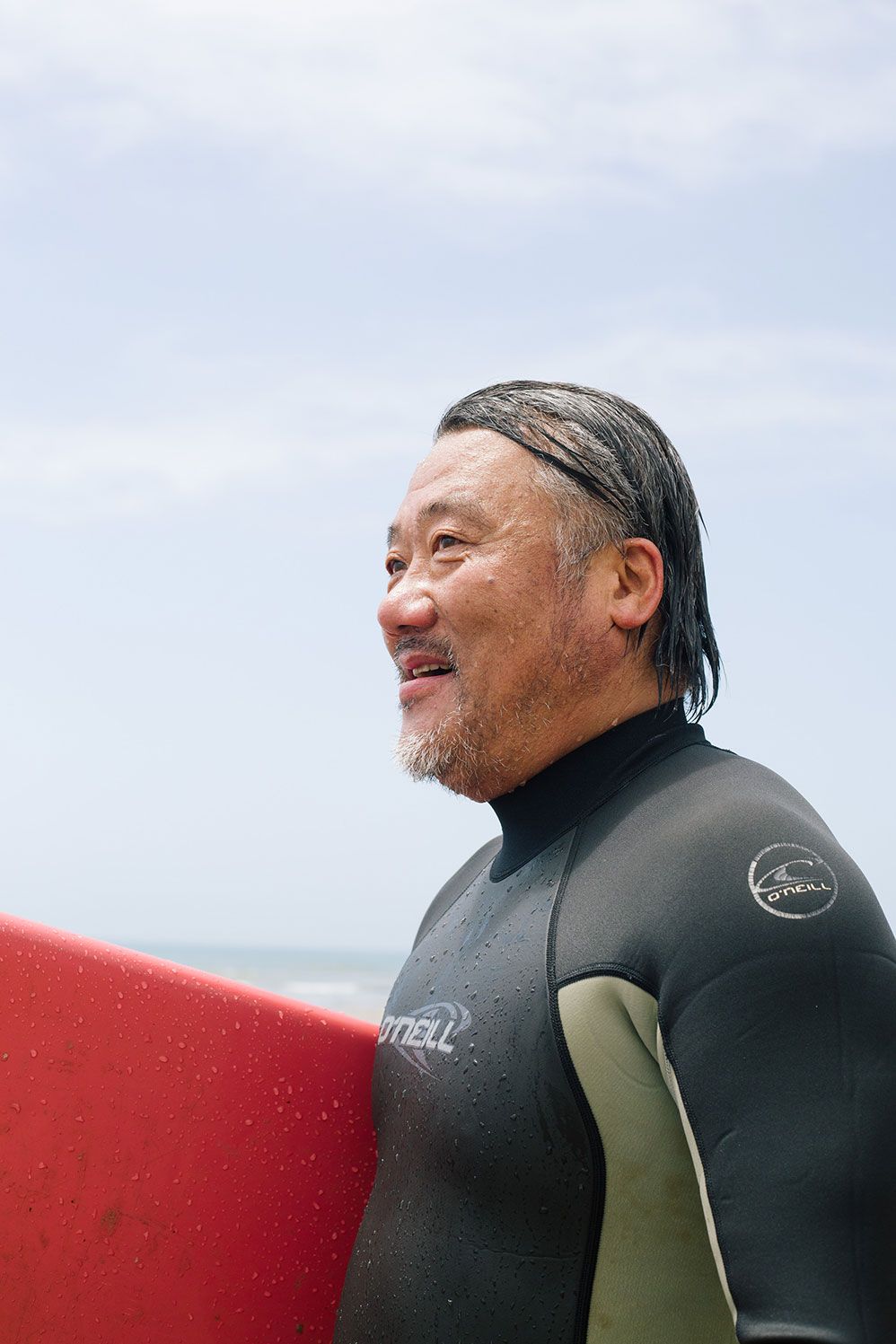 Smiling surfer in a wetsuit holding a red board on the beach