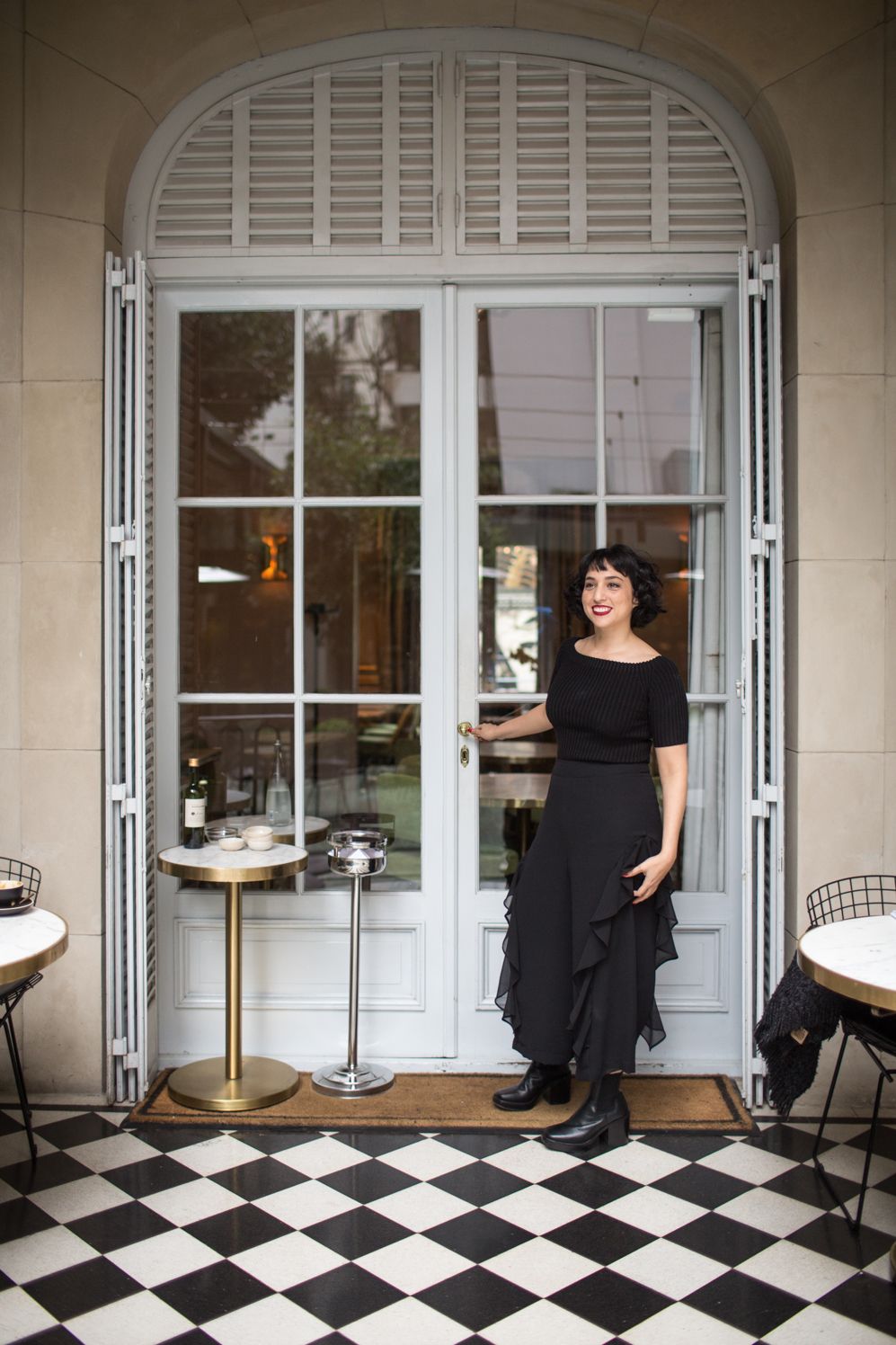 Woman in a black dress at an arched glass door above a black and white tiled floor