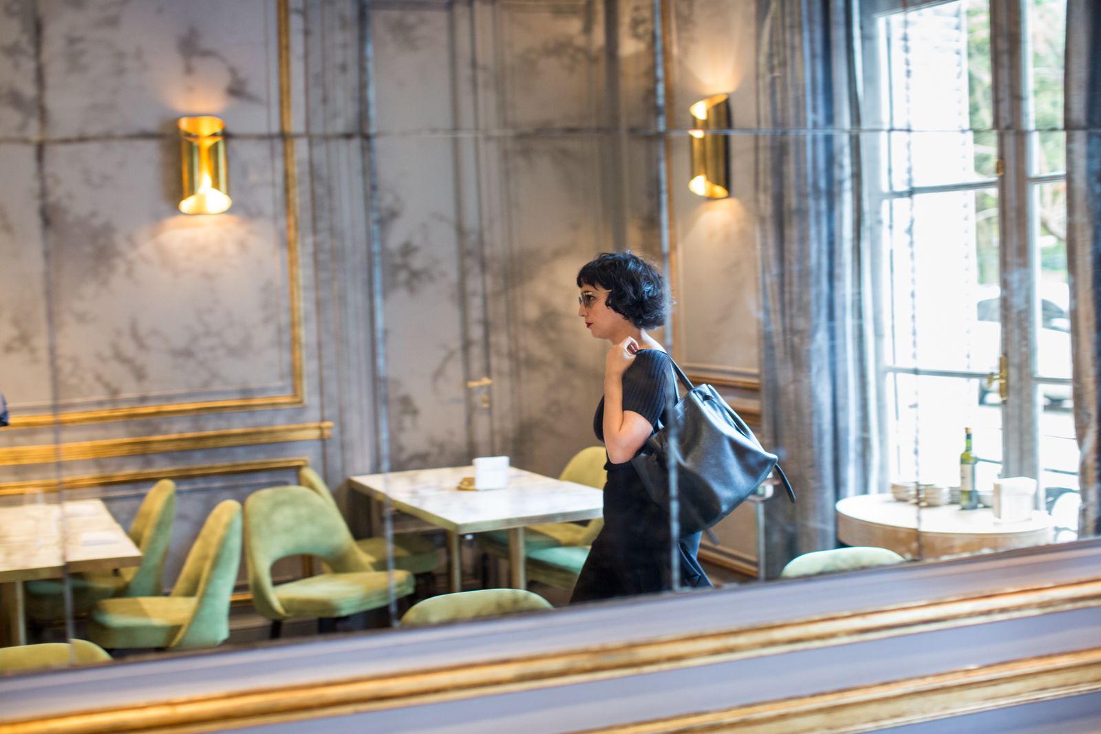 Woman with a shoulder bag walking through a café with gold wall lights and green velvet chairs, Buenos Aires
