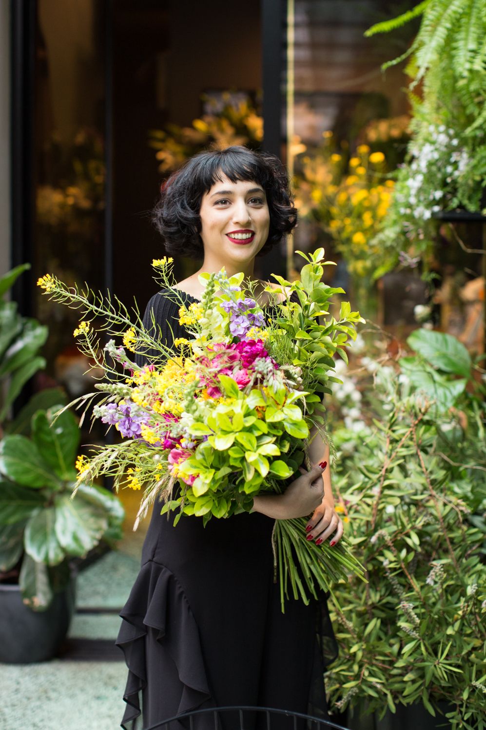 Woman holding a large bouquet of yellow and pink flowers in a green courtyard