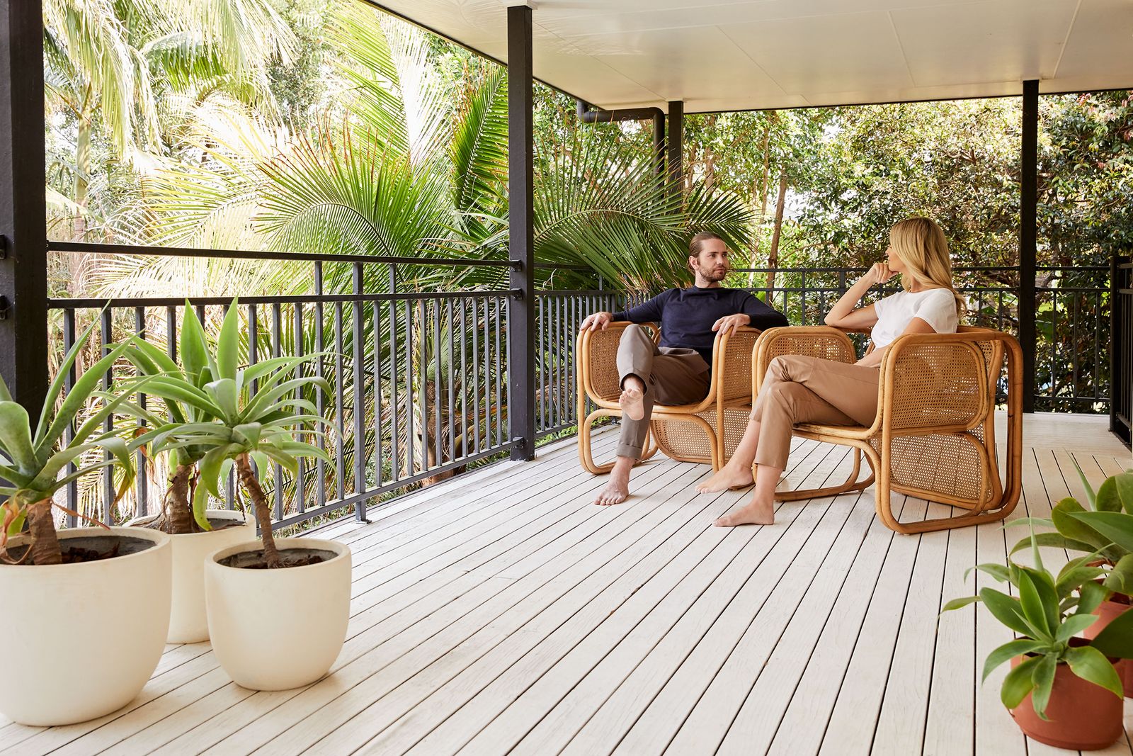 Couple in rattan chairs on a white wooden veranda surrounded by palms, Byron Bay