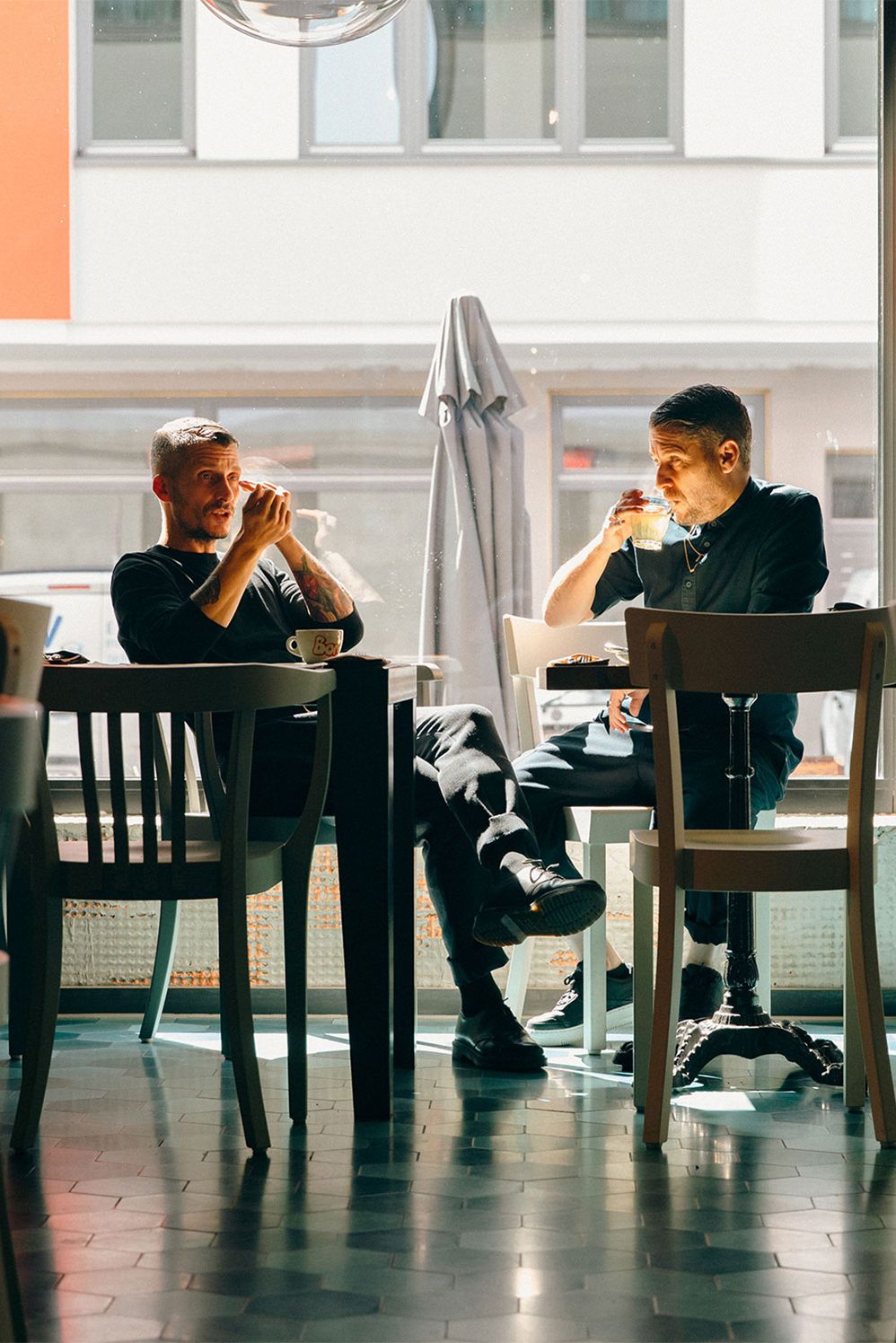 Two brothers talking over coffee at a table by a café window