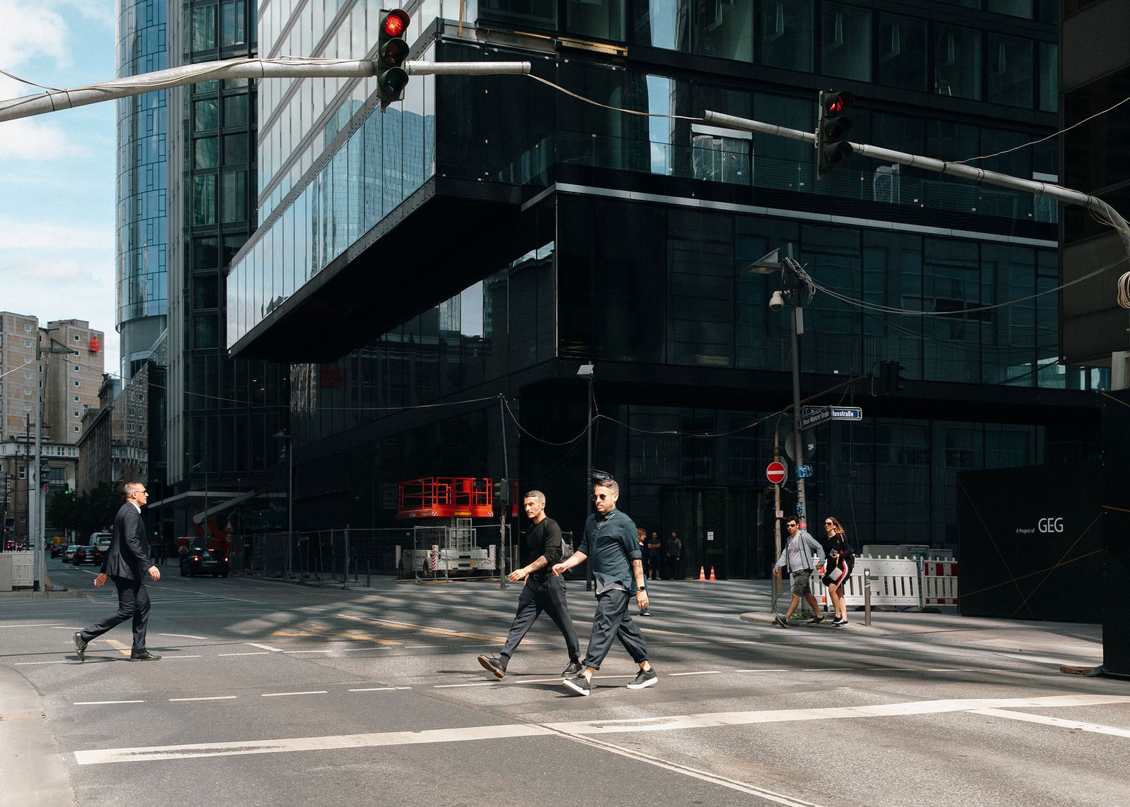 Two men in dark clothes crossing a street below glass towers in Frankfurt