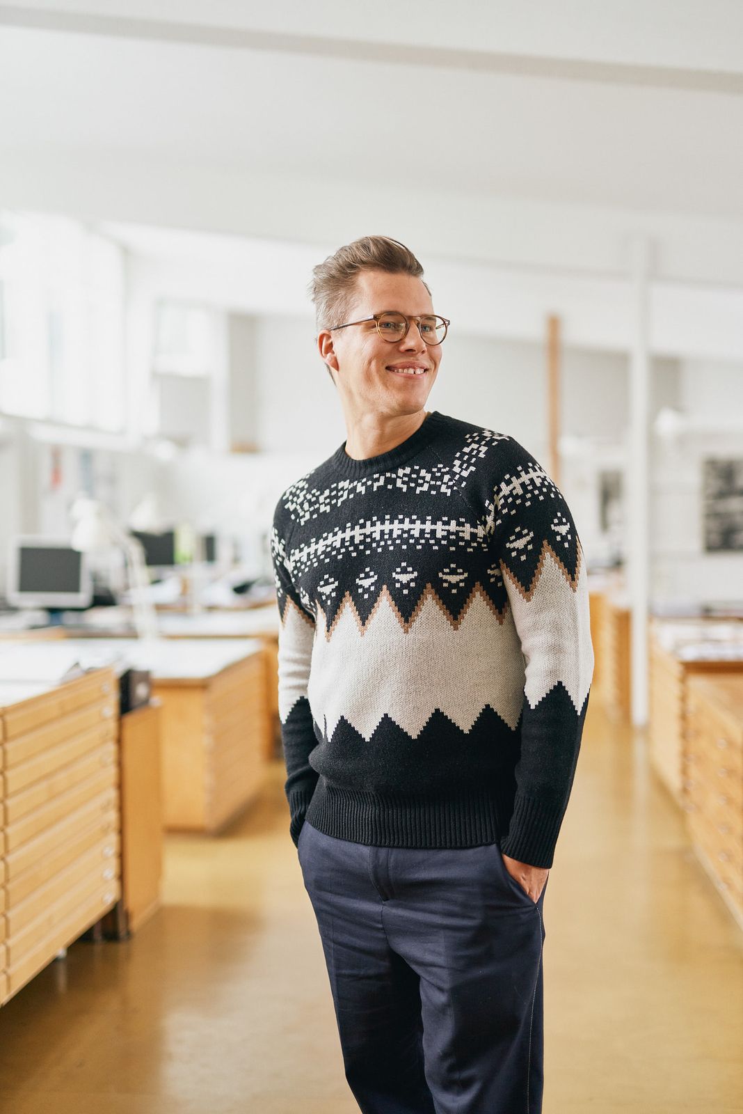 Designer in a black and white knit sweater standing in his studio