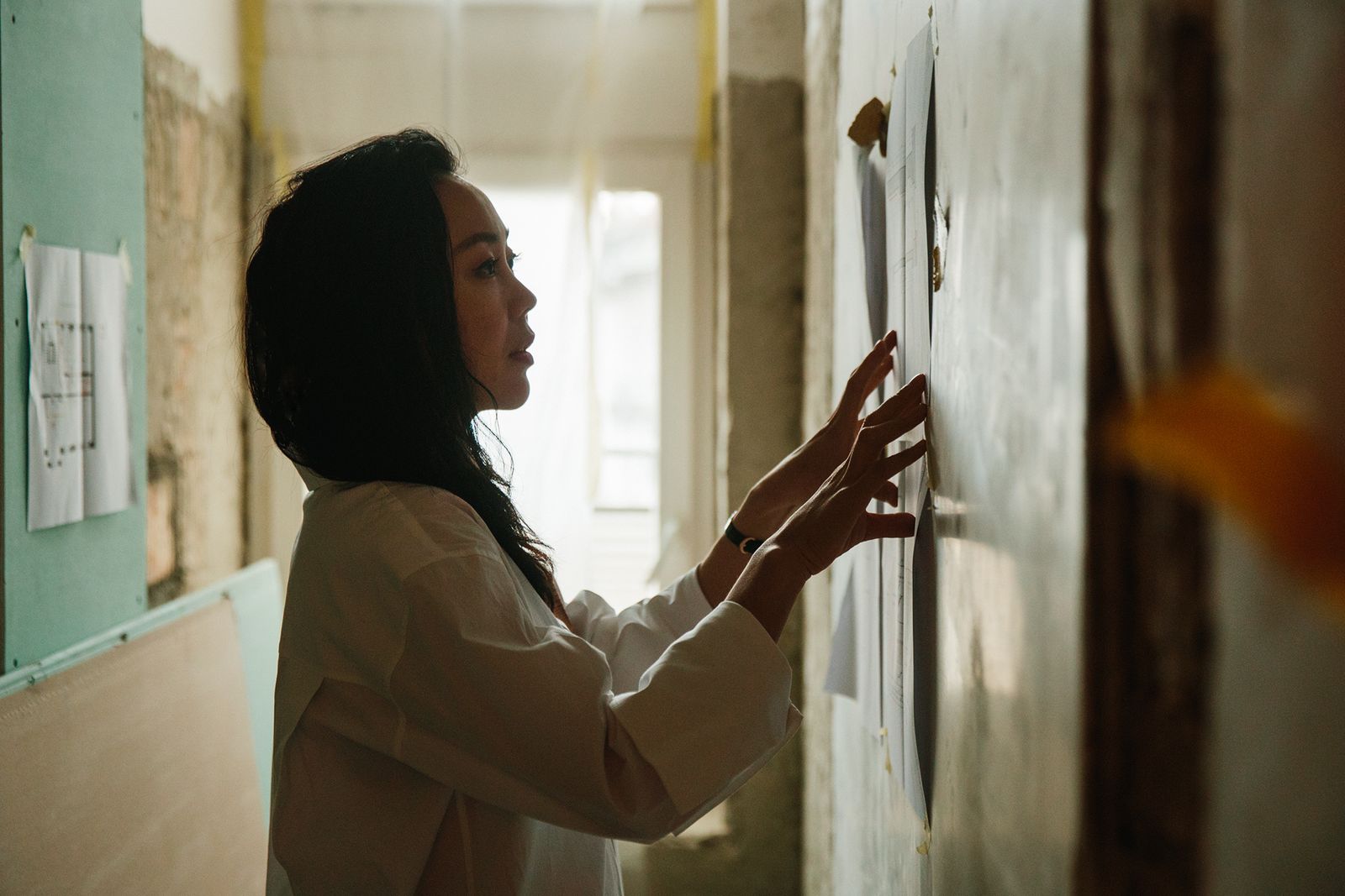 Architect Zhang Xi studying sketches pinned to a wall in the EXH Design office, Zurich