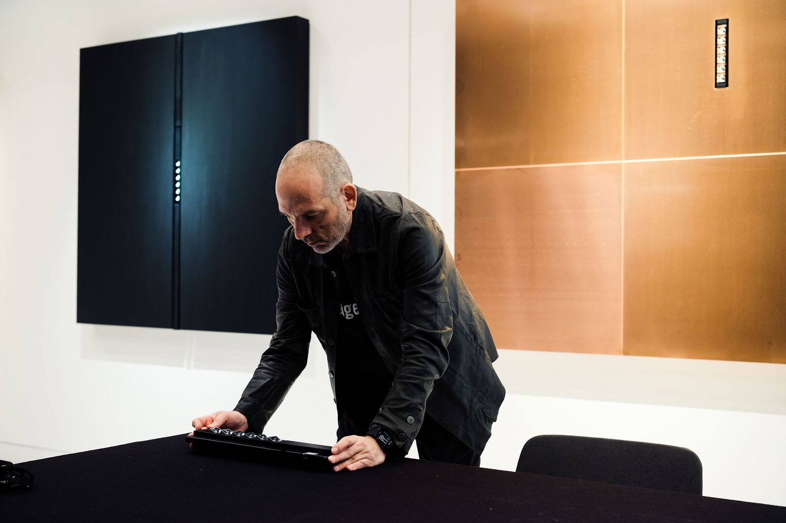 Designer Harald Gründl adjusting a lighting element in front of copper and black wall panels, Vienna