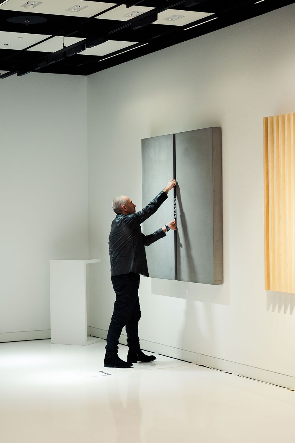Harald Gründl reaching up to a wall-mounted light installation in a white room