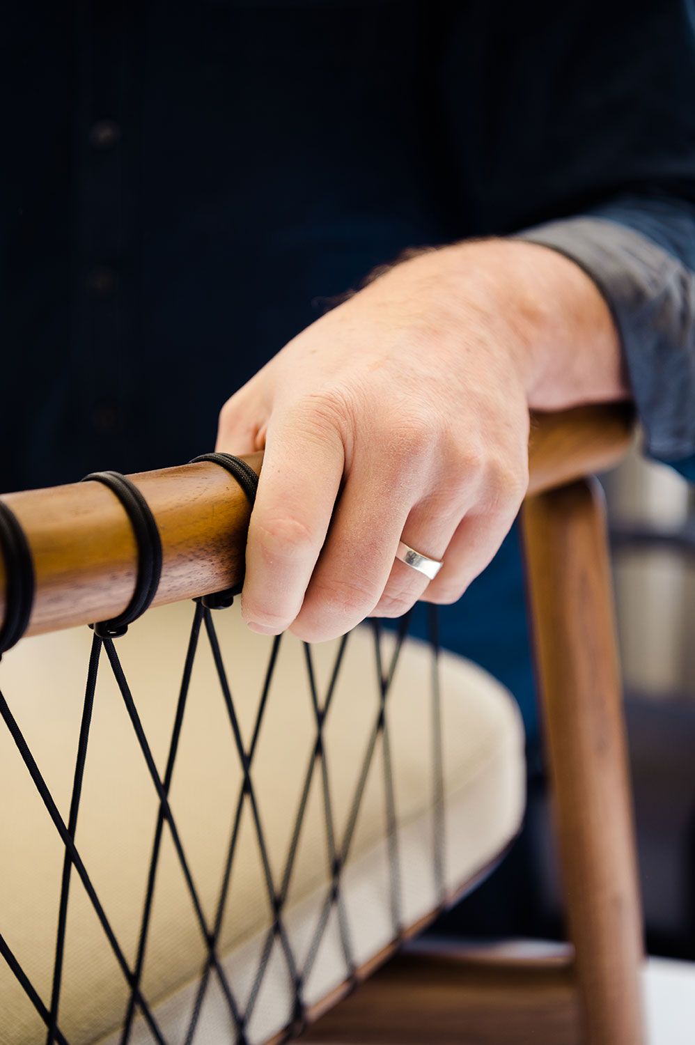 Hand resting on the wooden frame of a corded chair