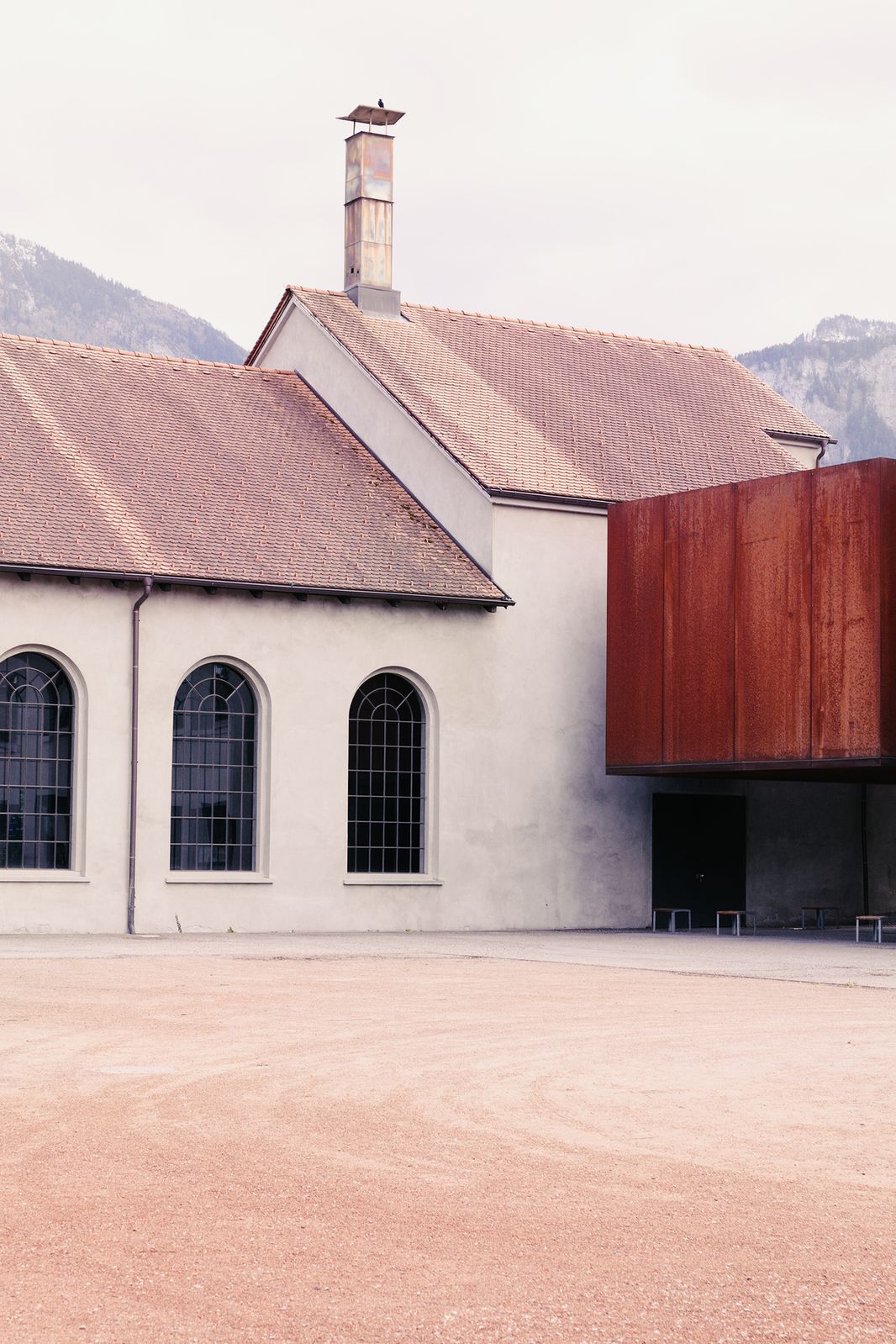 Whitewashed industrial hall with a rusted steel extension, Vorarlberg